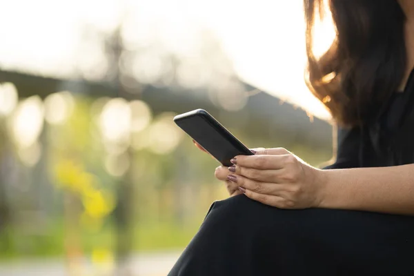 Close up hands woman using cell phone in public park. Adult female holding cell phone with beautiful sun light.