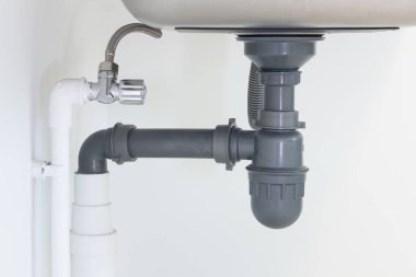 Kanalizasyon borusu ya da mutfak lavabosunun altı. PVC plastik boru ve paslanmaz çelik lavaboya esnek ikmal tüpü bağlantısı arasında musluk, drenaj suyu ve atık su ve tesisat sisteminde tuzak yer alıyor.