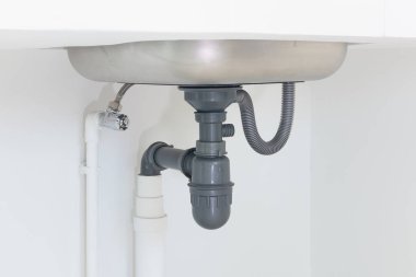 Kanalizasyon borusu ya da mutfak lavabosunun altı. PVC plastik boru ve paslanmaz çelik lavaboya esnek ikmal tüpü bağlantısı arasında musluk, drenaj suyu ve atık su ve tesisat sisteminde tuzak yer alıyor.