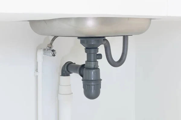 Drain pipe or sewer under kitchen sink. Pvc plastic pipe and flexible supply tube connection to stainless steel sink include faucet, trap for drain water and waste in drainage and plumbing system.