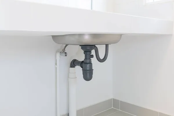 Drain pipe or sewer under kitchen sink. Pvc plastic pipe and flexible supply tube connection to stainless steel sink include faucet, trap for drain water and waste in drainage and plumbing system.