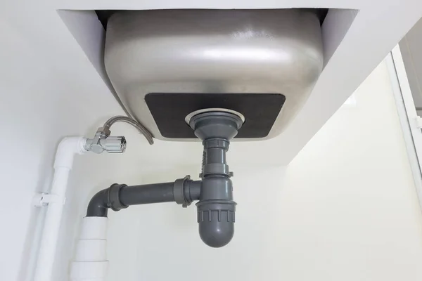 Drain pipe or sewer under kitchen sink. Pvc plastic pipe and flexible supply tube connection to stainless steel sink include faucet, trap for drain water and waste in drainage and plumbing system.