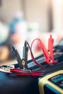 Charging electric power, energy to accumulator or dead battery in breakdown motorcycle or motorbike for start. Include equipment tool i.e. portable trickle charger, positive negative clamp, red black cable wire. May called recharge, check, repair.