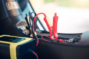 Charging electric power, energy to accumulator or dead battery in breakdown motorcycle or motorbike for start. Include equipment tool i.e. portable trickle charger, positive negative clamp, red black cable wire. May called recharge, check, repair.