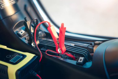 Charging electric power, energy to accumulator or dead battery in breakdown motorcycle or motorbike for start. Include equipment tool i.e. portable trickle charger, positive negative clamp, red black cable wire. May called recharge, check, repair.