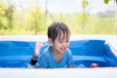 Asyalı çocuk, çocuk ya da küçük çocuk gülmek, banyo yapmak, su oynamak ya da yaz akşamları bahçedeki, bahçedeki, bahçedeki taşınabilir şişme yüzme havuzunda eğlenceli aktiviteler yapmak. Yeşil alanı, gökyüzü arkaplanını dahil et.