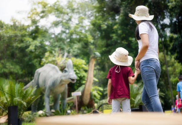 stock image Mother to adventure travel in history park with son, asian child, kid or little boy. Include dinosaur sculpture, grass, field, landscape at outdoor garden. Caucasian family from Chiang Mai, Thailand.