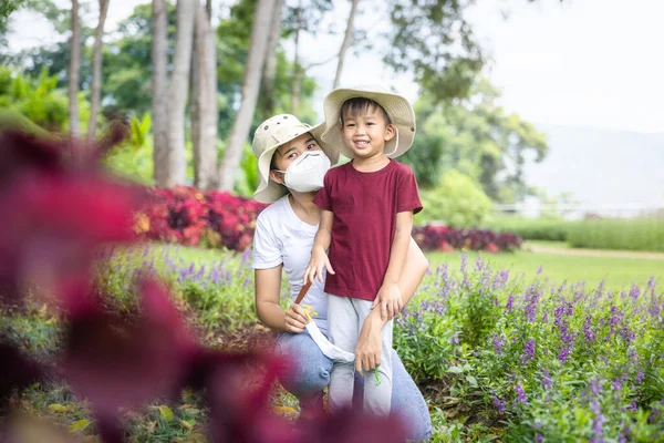 Mom holding son, kid or little boy at outdoor. Include forget-me-not flower in garden. Look cut, fun, happy. He is caucasian, asian child in thailand. Concept of love, family, care and relationship.
