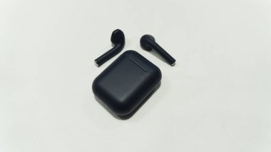 Kablosuz mavi kulaklıklar bir yana beyaz arka planda şarj aletlerinin yanında.