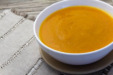 Thick and Creamy Pumpkin Soup in white bowl on wooden rustic background, linen napkin. Healthy eating, horizontal.