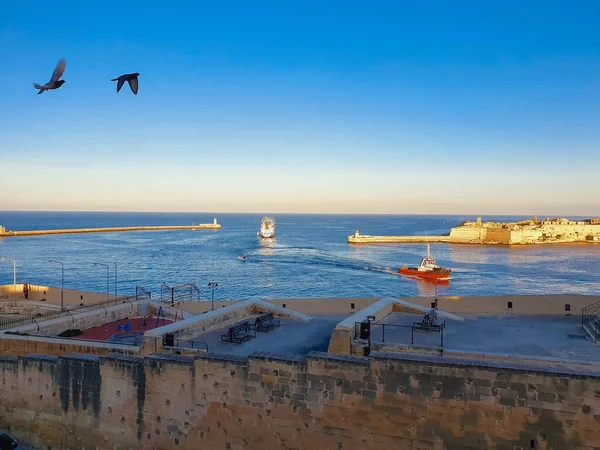 Pohled na starý maják Saint Elmo, Valletta, Malta, Středozemní moře, Světlá věž. Horizontální tapetový nápis krytu makety. Úžasný výhled na moře, lodě plují na moři, ptáci na obloze — Stock fotografie