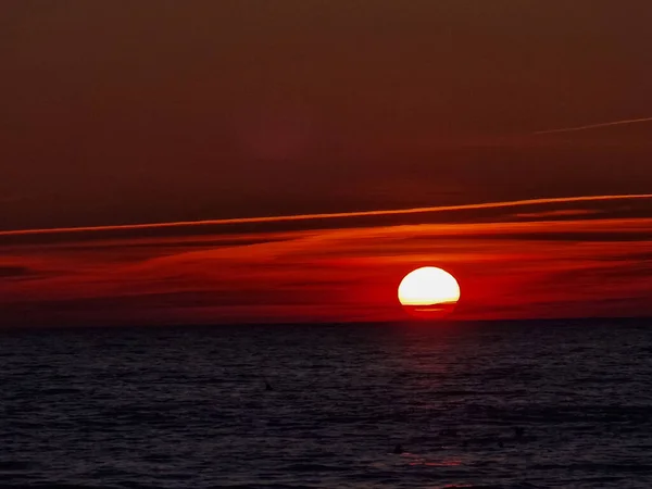 Una puesta de sol ardiente de color rojo oscuro sobre el mar con un reflejo rojo en la superficie del agua. Cielo dramático. Para su diseño, calendario, postal, papel de regalo, papel pintado, tarjeta de felicitación, postal, banner —  Fotos de Stock