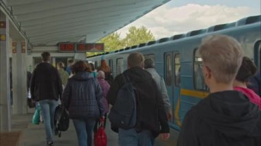 Bir sürü insan işten metroyla eve gider. Kalabalık bir akıntı, hareket halindeki metro treninin yanındaki çıkışa gidiyor. Kyiv metrosunun zemin istasyonundaki saatler. Yavaş Hareket 100fps 2.8k