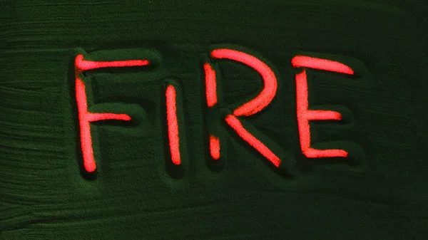 Hand drawing the Word Fire in the Green Sand. Male hand writes the word Fire on the green sand with red backlight. Top view 4k resolution