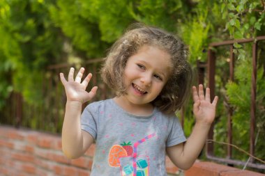 Bahçedeki kırmızı tuğla duvarın önünde neşeyle gülümseyen küçük kız.