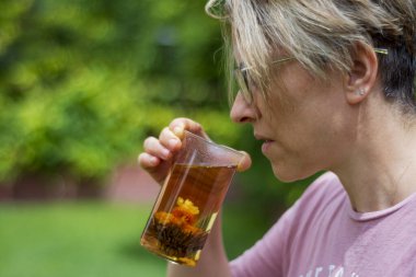 Gözlüklü genç kadın evinin bahçesinde çiçek açan çayını içiyor, Seçici Odak Cam.