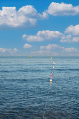 Dalgalı deniz yüzeyi ve turuncu işaretli dubalar. Uzakta küçük bir balıkçı teknesi. Seçici Odaklanma. İnsan Yok.