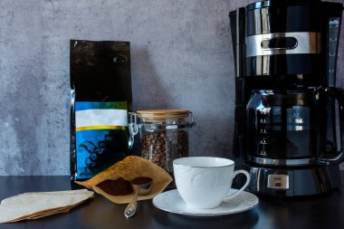 Kahve makinesi, bir fincan, kahve çekirdeği dolu bir kavanoz ve bir kaşık filtre kahve..