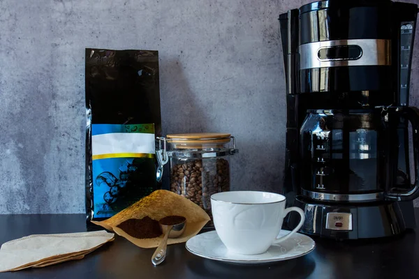 Kahve makinesi, bir fincan, kahve çekirdeği dolu bir kavanoz ve bir kaşık filtre kahve..