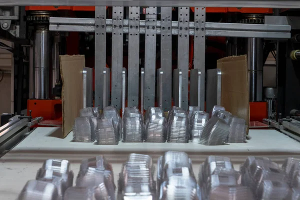 Fabrikada vakum termoformasyon makinesi kullanılıyor, vakum termoform makinesi plastik ambalaj üretimi için kullanılıyor. Kalıplı plastik kapların yakın görüntüsü. Seçici odak paketleme.