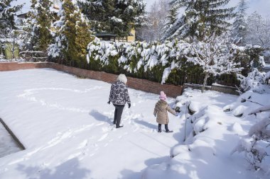 Genç bir kadın ve küçük kızı evlerinin karla kaplı bahçesinde yürüyorlar. Ayak izleriyle bir şeyler çizmeye çalışıyorlar. Kalp Şekli.