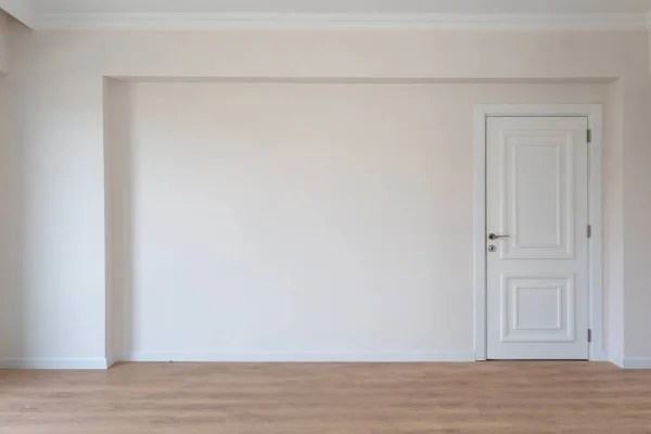 房间里空荡荡的 公寓里有香槟酒色的墙壁和木制的地板 墙上右边有白色的木门 图库照片