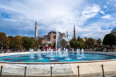 İstanbul, Türkiye - 27-09-2022: İstanbul 'un Sultanahmet Meydanı' ndaki Ayasofya camii manzarası aydınlık yaz günü. Ayasofya 'nın arkasındaki havuzda parktaki çeşmeden su fışkırıyor.