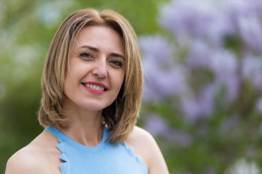 Otuz yaşından büyük mutlu bir kadının portresi çiçek açan ağaçların bulanık arka planında. Metin için kopyalama alanı