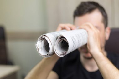 Elinde iki tane çarpık gazete tutan adam. Dürbünlü metafor ya da alegori. Seçici olarak gazetelere odaklan. Gerçek arama konsepti