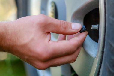 El, arabanın tekerleğindeki meme ucu kapağını büker ya da açar. Havalandırma lastiklerini yerleştirin. Metin veya harf için kopyalama alanı olan ayarlanmış arkaplan.