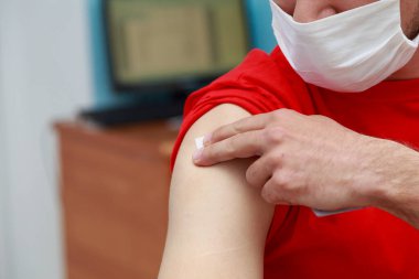 Hasta yamaya basarken elini enjeksiyon yerinde tutuyor. Covid-19 koronavirüse karşı gerçek aşı. Arkaplan