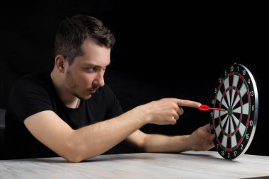 Siyah elbiseli genç yakışıklı bir adam ve ortasında siyah bir arka planda bir dart tahtası olan bir dart tahtası. Hedef başarı konsepti