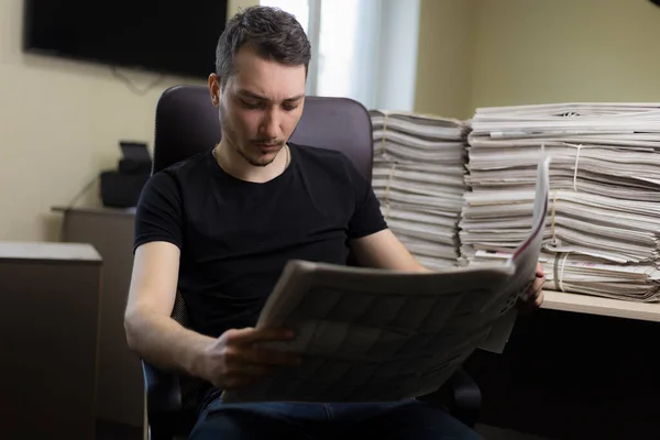 Młody Człowiek Czytający Gazetę Niewyraźnym Tle Biurowym — Zdjęcie stockowe