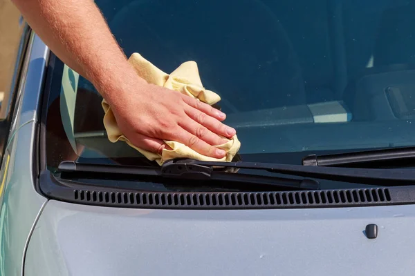 A hand with a dry rag wipes the windshield of a car at a car wash. Background with copy space for text or lettering.