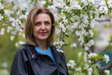 Otuz yaşından büyük mutlu bir kadının portresi çiçek açan ağaçların bulanık arka planında. Metin için kopyalama alanı