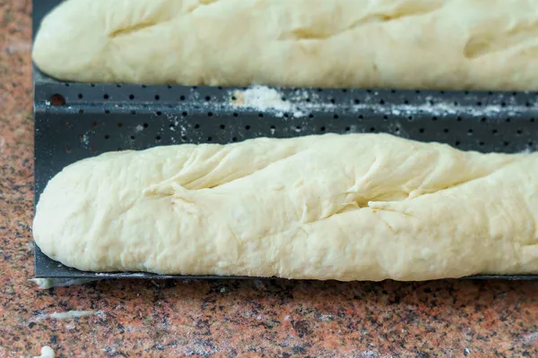 Dough in the kitchen. French baguettes on a baking sheet. Homemade bread baking. Background with selective focus and copy space for text