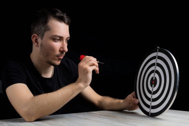 Siyah elbiseli genç yakışıklı bir adam ve gösterişsiz bir dart tahtası. Hedef başarı konsepti