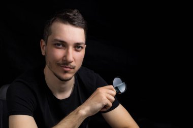 Genç yakışıklı bir adam ve siyah arka planda gösterişsiz bir büyüteç. Arama sembolü. Soruşturma kavramı