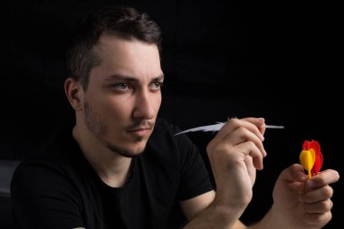 Kaz tüyü giymiş siyah giysili genç yakışıklı bir adam, siyah arka planda gizli bir dart metaforu. Hedef belirleme kavramı