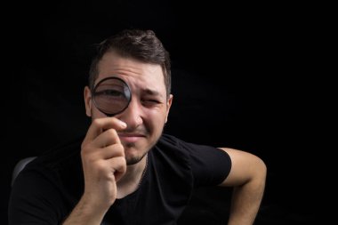Genç yakışıklı bir adam ve siyah arka planda gösterişsiz bir büyüteç. Arama sembolü. Soruşturma kavramı