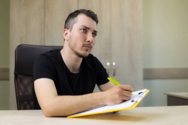 Genç, yakışıklı bir adam ya da yetişkin bir adam ofisin bulanık bir arka planı üzerinde çalışıyor..