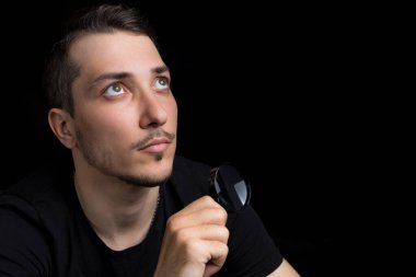 Genç yakışıklı bir adam ve siyah arka planda gösterişsiz bir büyüteç. Arama sembolü. Soruşturma kavramı