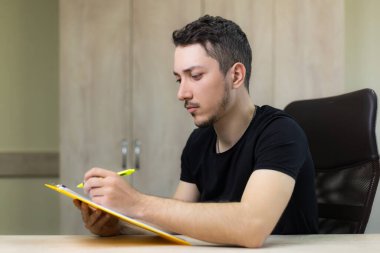 Genç, yakışıklı bir adam ya da yetişkin bir adam ofisin bulanık bir arka planı üzerinde çalışıyor..