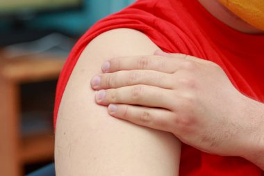 Hasta yamaya basarken elini enjeksiyon yerinde tutuyor. Covid-19 koronavirüse karşı gerçek aşı. Arkaplan