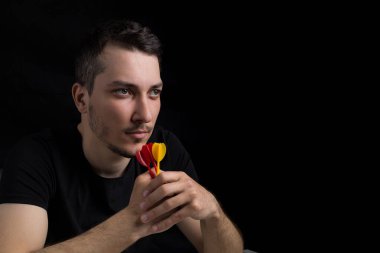 Siyah elbiseli, elinde dartlarla siyah arka planda, sade bir anahtarla dolaşan yakışıklı bir genç. Hedefe hazır olma kavramı