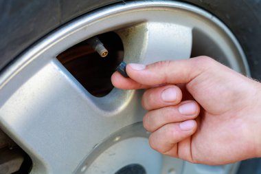 El, arabanın tekerleğindeki meme ucu kapağını büker ya da açar. Havalandırma lastiklerini yerleştirin. Metin veya harf için kopyalama alanı olan tonlanmış arkaplan. Meme ucuna odaklan..