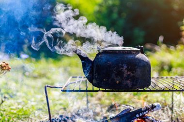 Ateşin üstünde siyah bir karbon tabakası olan çok eski bir çaydanlık. Turist kampında yürüyüş yaparken. Kopyalama alanı olan arkaplan