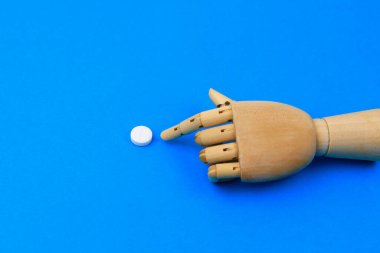 Ahşap bir el geleneksel mavi arka planda puanı olan klasik bir beyaz hapa işaret eder. Metin için kopyalama alanı olan haplara seçmeli odaklan