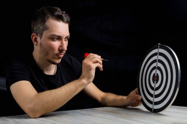 Siyah elbiseli genç yakışıklı bir adam ve gösterişsiz bir dart tahtası. Hedef başarı konsepti