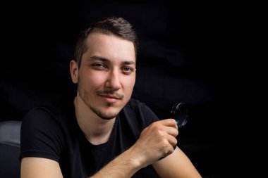 Genç yakışıklı bir adam ve siyah arka planda gösterişsiz bir büyüteç. Arama sembolü. Soruşturma kavramı